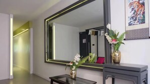 Ένα σύγχρονο δωμάτιο ξενοδοχείου με έναν μεγάλο καθρέφτη, ένα μικρό τραπέζι με ένα βάζο λουλούδια και έναν πίνακα με την εικόνα μιας τίγρης που είναι τοποθετημένος στον τοίχο.