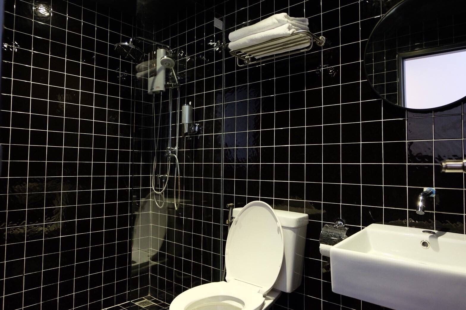 Une salle de bain avec des murs recouverts de carreaux noirs, des toilettes blanches, un lavabo et une douche.