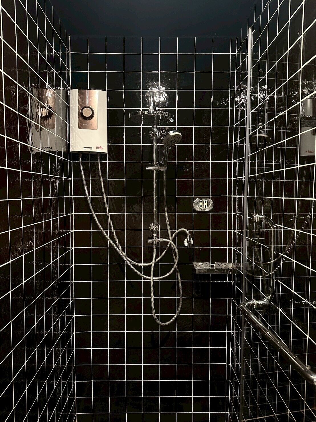 Een badkamer met zwart betegelde wanden, een douche met een handdouche en een bedieningspaneel.
