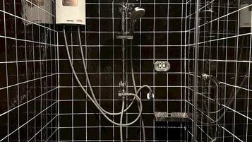 Een badkamer met zwart betegelde wanden, een douche met een handdouche en een bedieningspaneel.