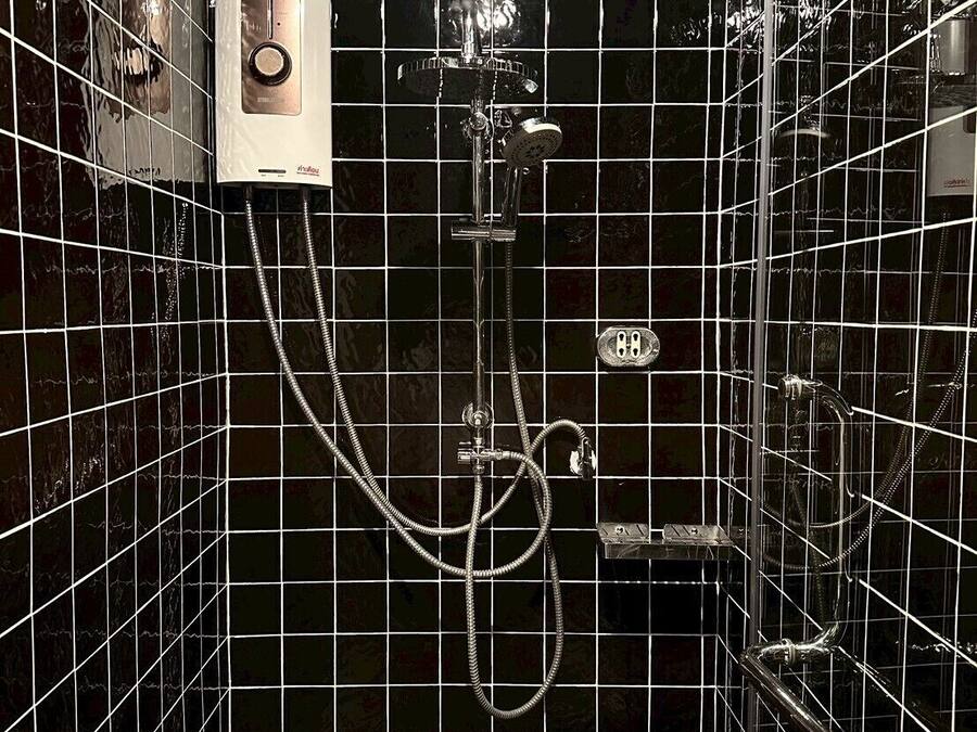 Een badkamer met zwart betegelde wanden, een douche met een handdouche en een bedieningspaneel.