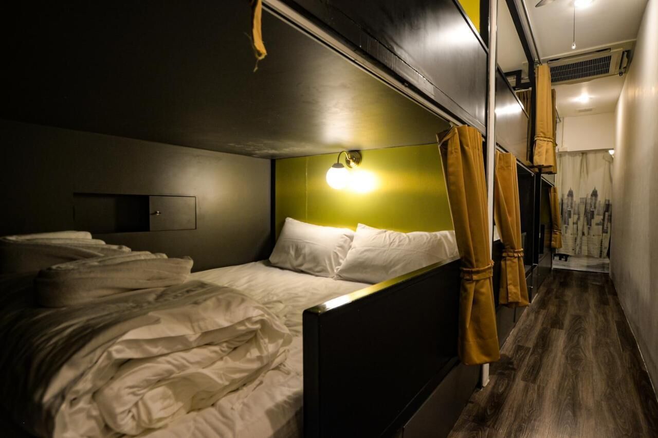 A single bed with white bedding in a room with a green accent wall and a ceiling light.