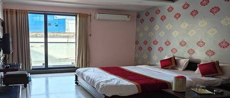 A hotel room with a bed, a desk, a chair, a table, a ceiling fan, and a large window.