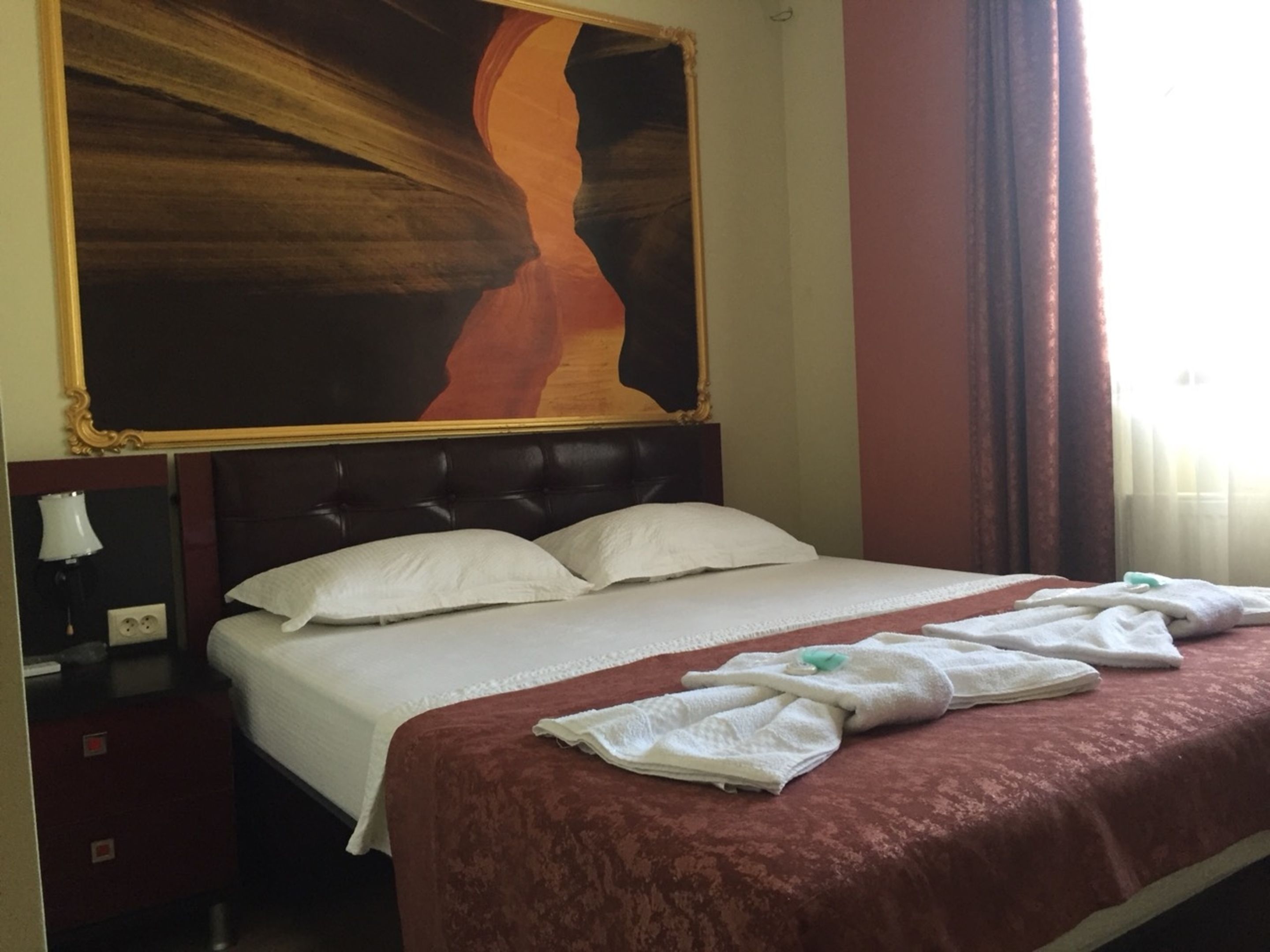 A hotel room with a large bed, a nightstand, a lamp, and a painting on the wall.