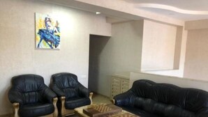 Uma sala de estar com dois poltronas de couro preto, uma mesa de centro de madeira com peças de xadrez e um amplo sofá de couro preto.
