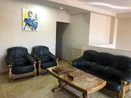 A living room with two black leather armchairs, a wooden coffee table with chess pieces, and a large black leather sofa.