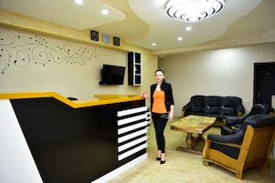 Un área de recepción con un mostrador negro y amarillo, un televisor de pantalla plana, un sofá y una mesa de centro de madera.