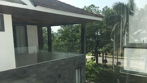 A modern building with a balcony overlooking a green area with trees and a road.