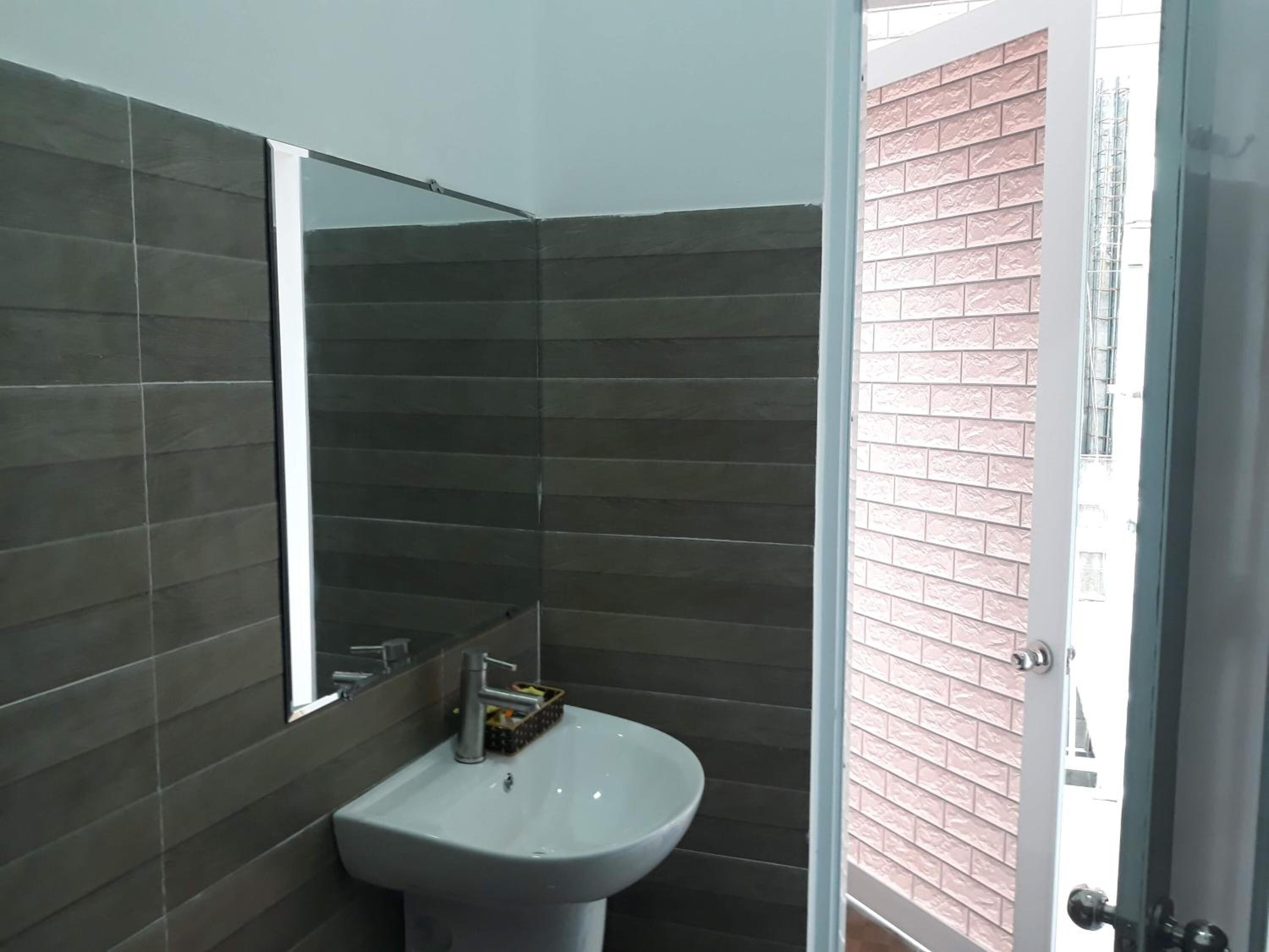 A bathroom with dark tiled walls, a white sink, and a mirror.
