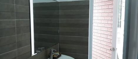 A bathroom with dark tiled walls, a white sink, and a mirror.