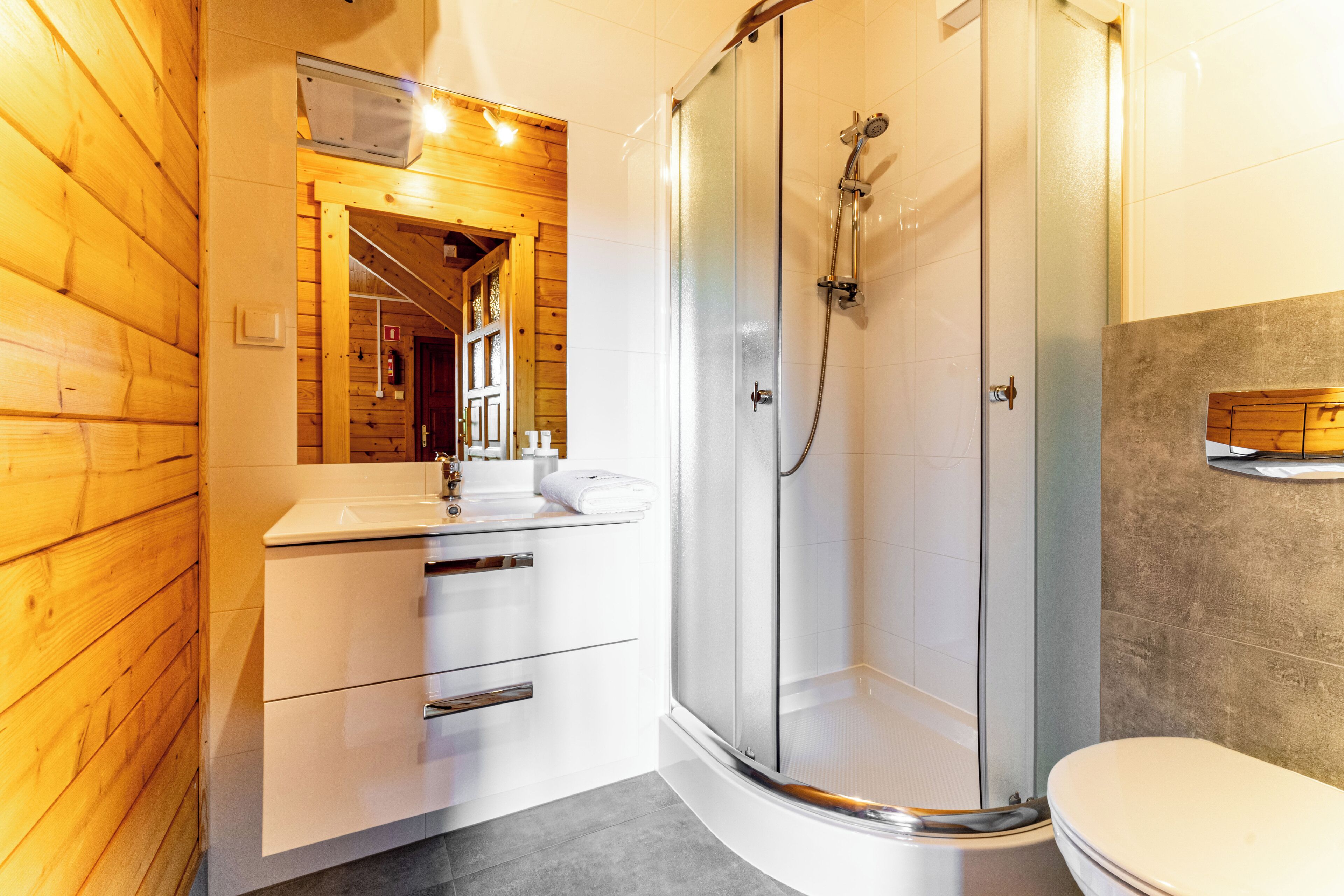 A modern bathroom with a glass-enclosed shower, a wooden vanity, and a white toilet.