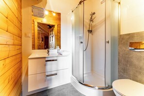 A modern bathroom with a glass-enclosed shower, a wooden vanity, and a white toilet.