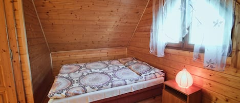 A wooden cabin room with a bed, a nightstand, and a window with curtains.