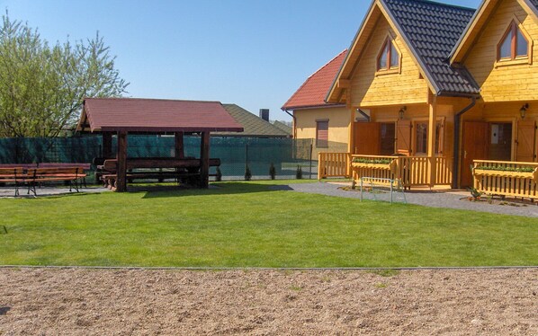 A wooden cabin with a red roof, a covered picnic area, and a well-maintained lawn.
