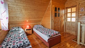 A wooden cabin room with two beds, a nightstand, and a door with a window. - Domki Agat (Sarbinowo)