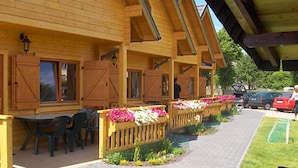 A wooden building with a covered patio area, outdoor seating, and flower planters. - Domki Agat (Sarbinowo)