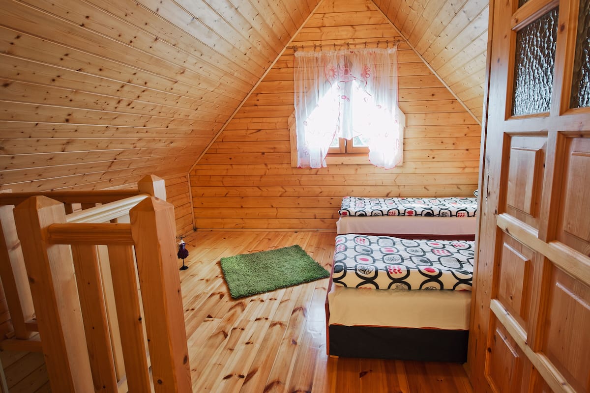 A wooden-paneled attic bedroom with a bed, a small rug, and a window with sheer curtains.