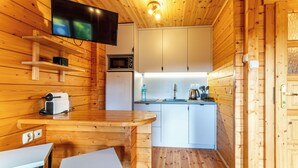A compact kitchen with wooden walls, a flat-screen TV mounted above the counter, and basic appliances including a microwave and refrigerator. - Domki Agat (Sarbinowo)