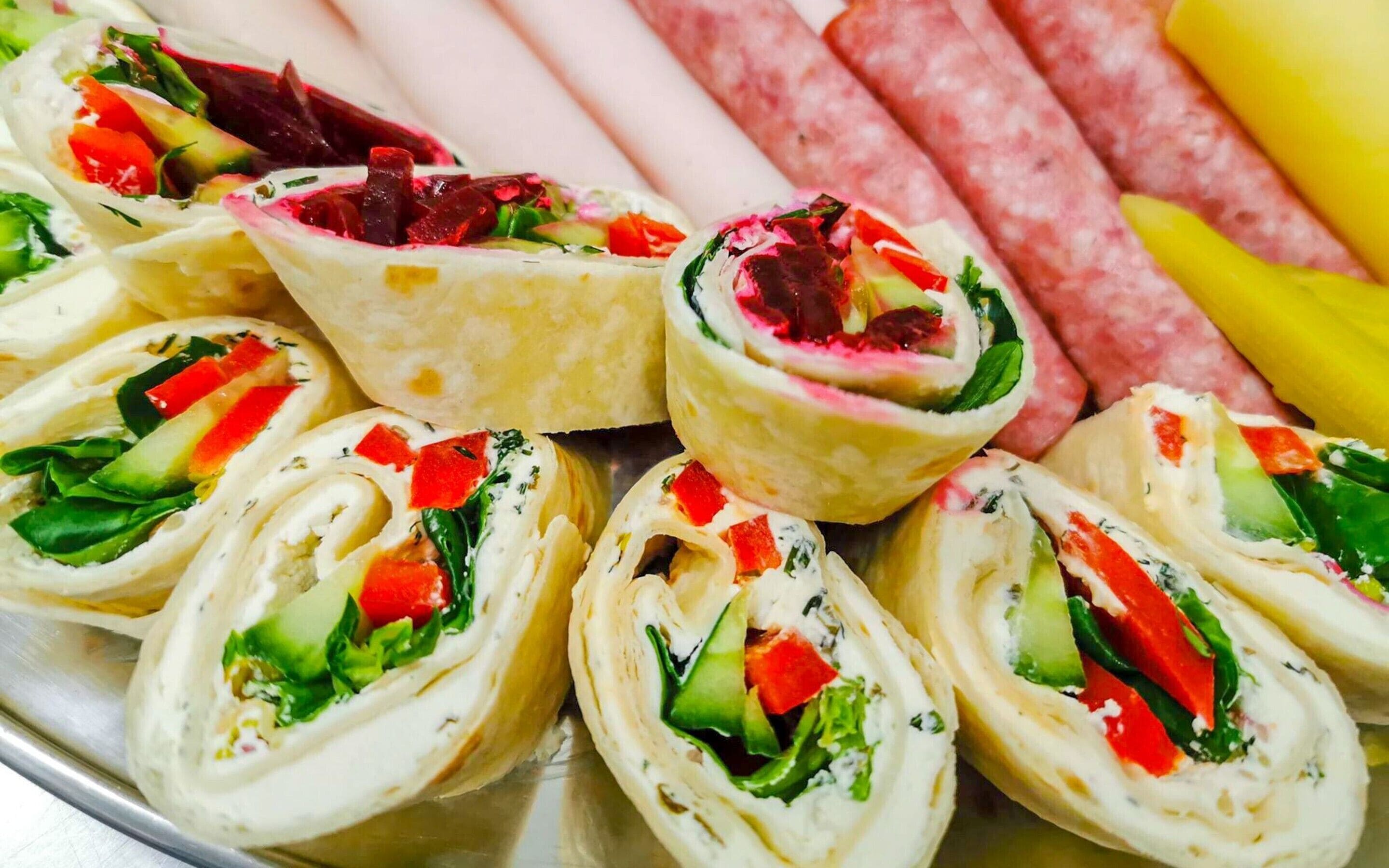 A tray of food items including wraps with vegetables and meat, and slices of sausage.