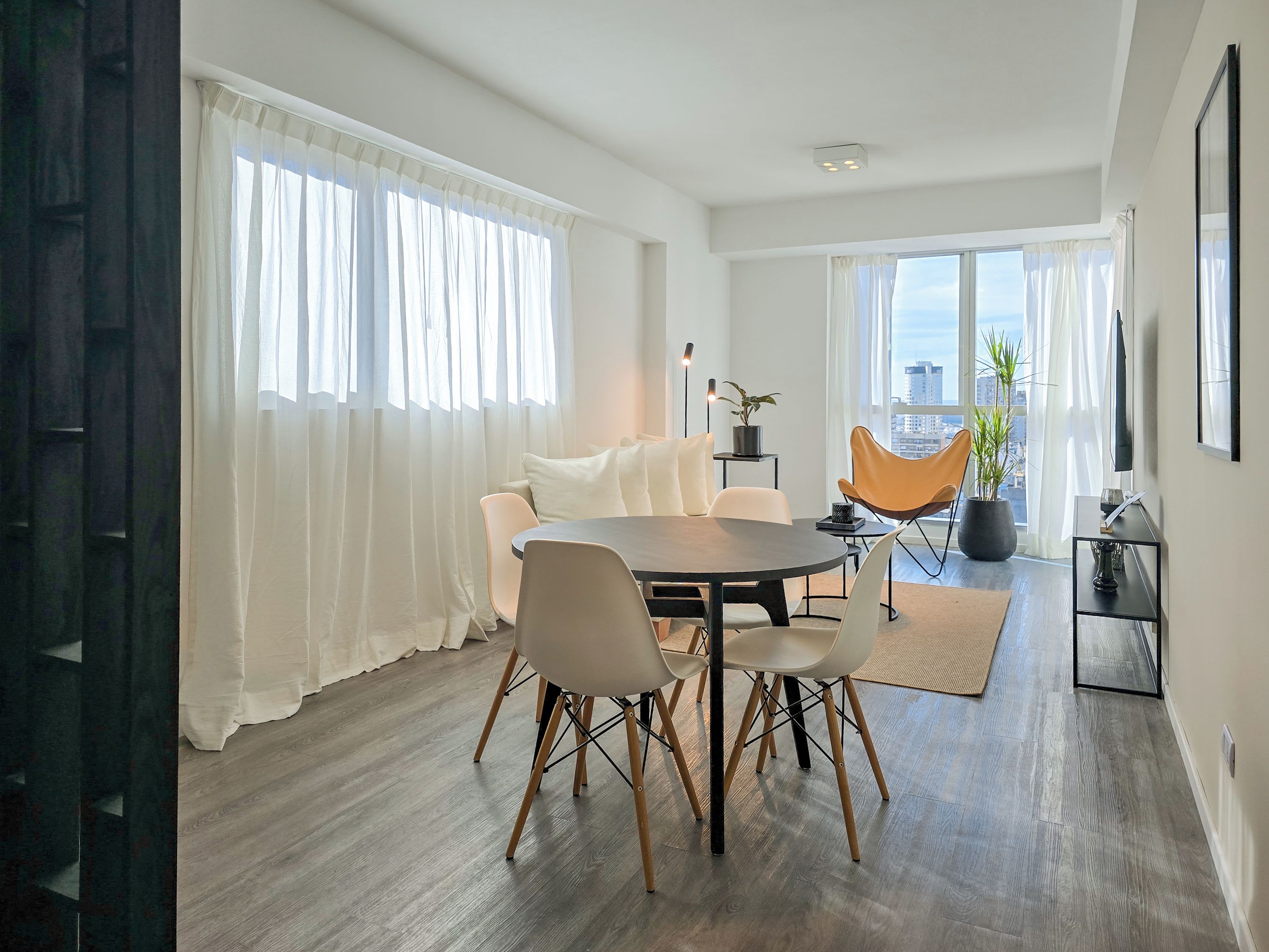A modern dining area with a round table, chairs, and a view of the city through large windows.