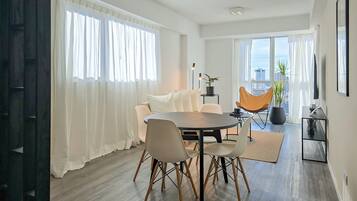 A modern dining area with a round table, chairs, and a view of the city through large windows.