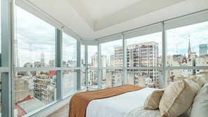 A modern bedroom with a large bed, a view of the cityscape through floor-to-ceiling windows, and a city skyline visible outside. - Nido x Bellini Esmeralda (Buenos Aires)
