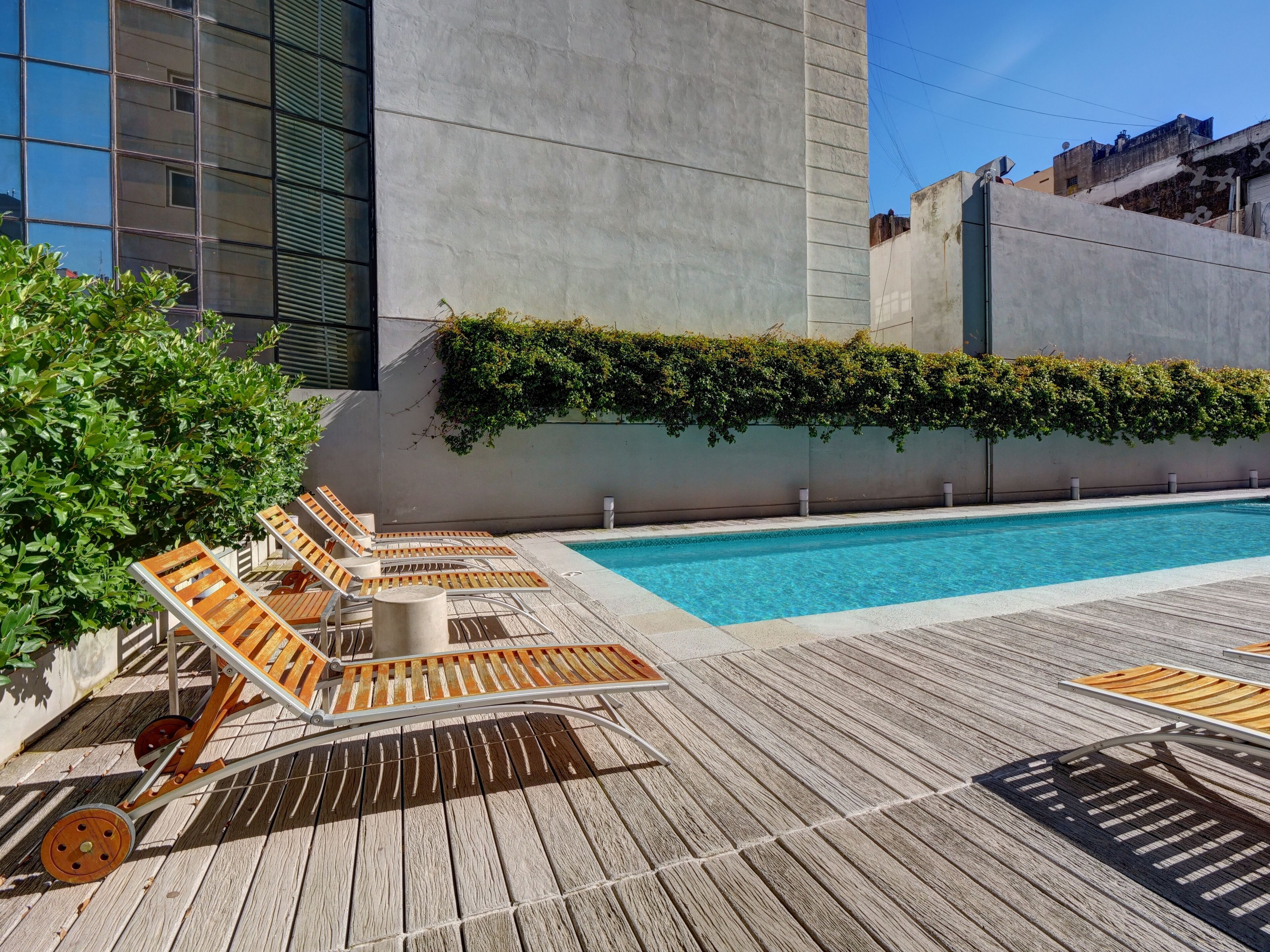 Un espace piscine aménagé sur le toit, avec des chaises longues en bois et une piscine.