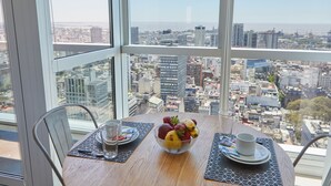 A table with a fruit bowl, a cup, and a glass, overlooking a cityscape with buildings and a view of the ocean. - Nido x Bellini Esmeralda (Buenos Aires)