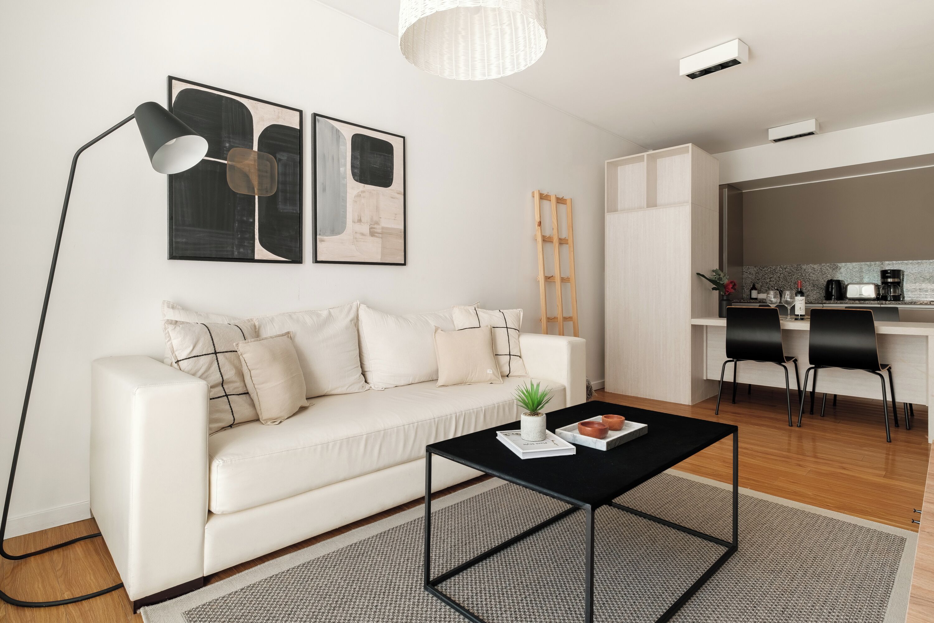 A modern living room with a white sofa, a black coffee table, and a kitchen area with a white countertop and black chairs.