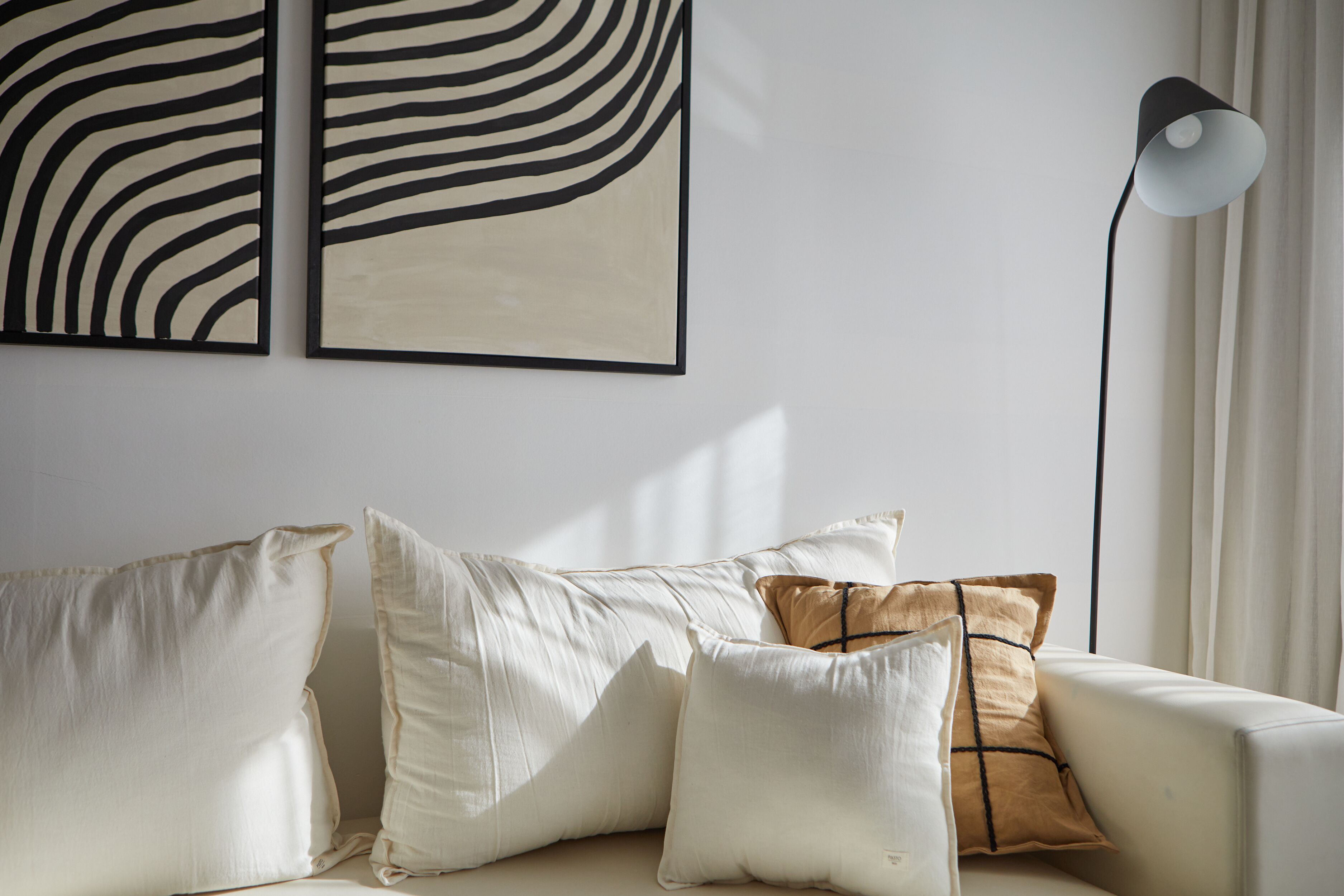 A modern living room with a sofa, cushions, and two abstract wall art pieces.