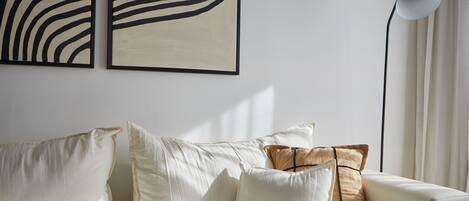 A modern living room with a sofa, cushions, and two abstract wall art pieces.