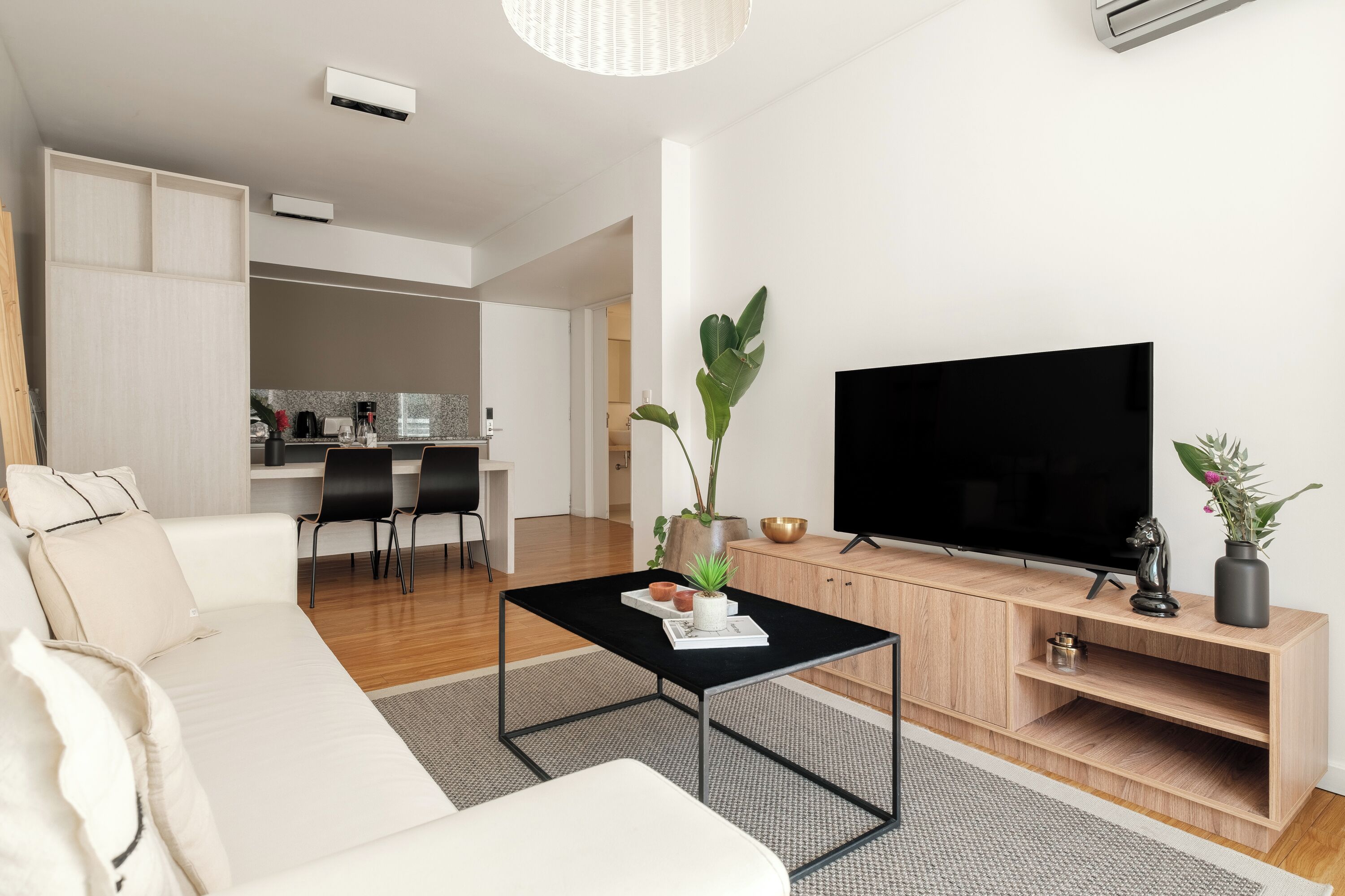 A modern living room with a black coffee table, a sofa, a TV on a wooden stand, and a dining area in the background.