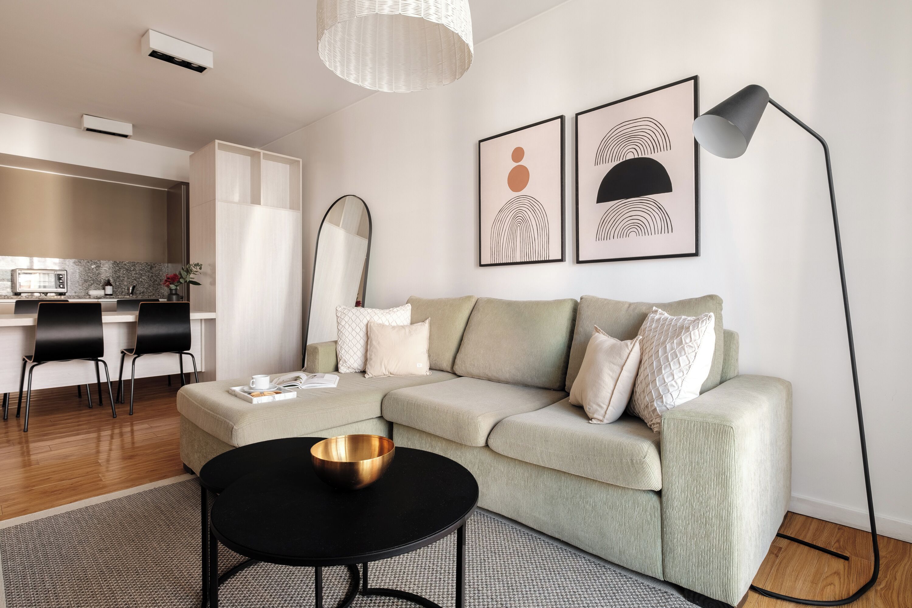 A modern living room with a sofa, a coffee table, and a dining area with chairs and a kitchen in the background.