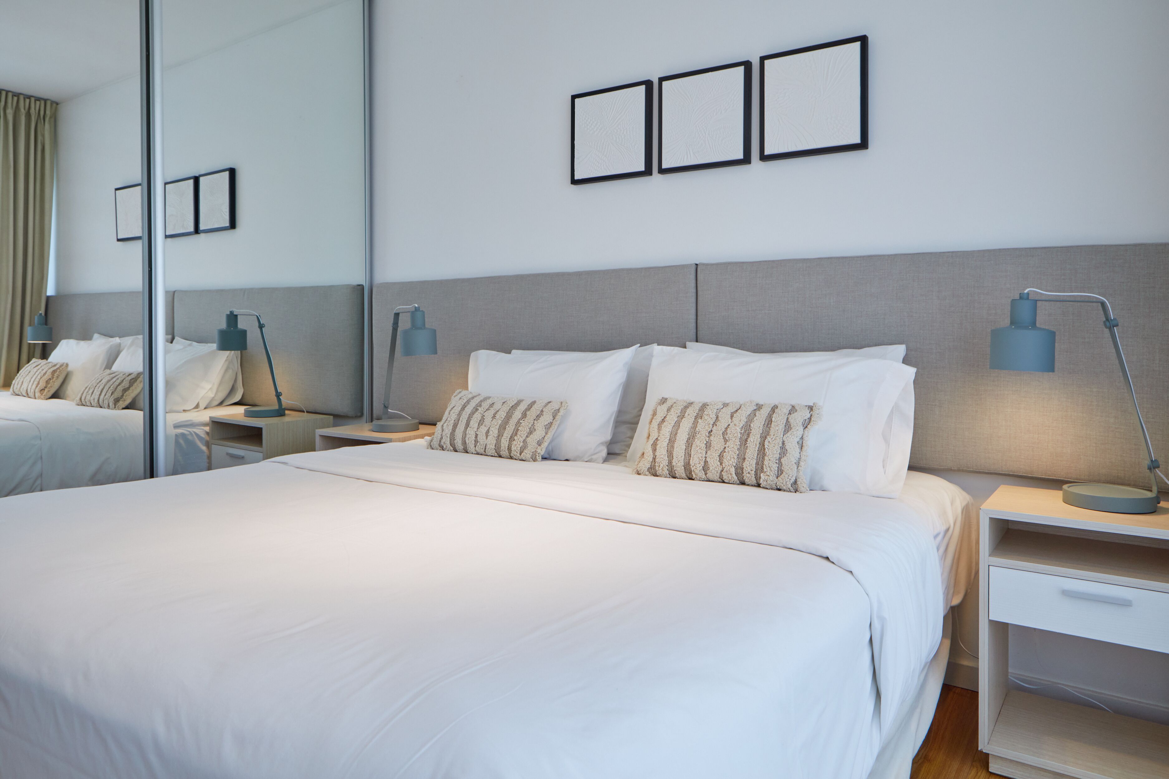 A modern hotel room with a large bed, two bedside tables, a nightstand, and a mirror.