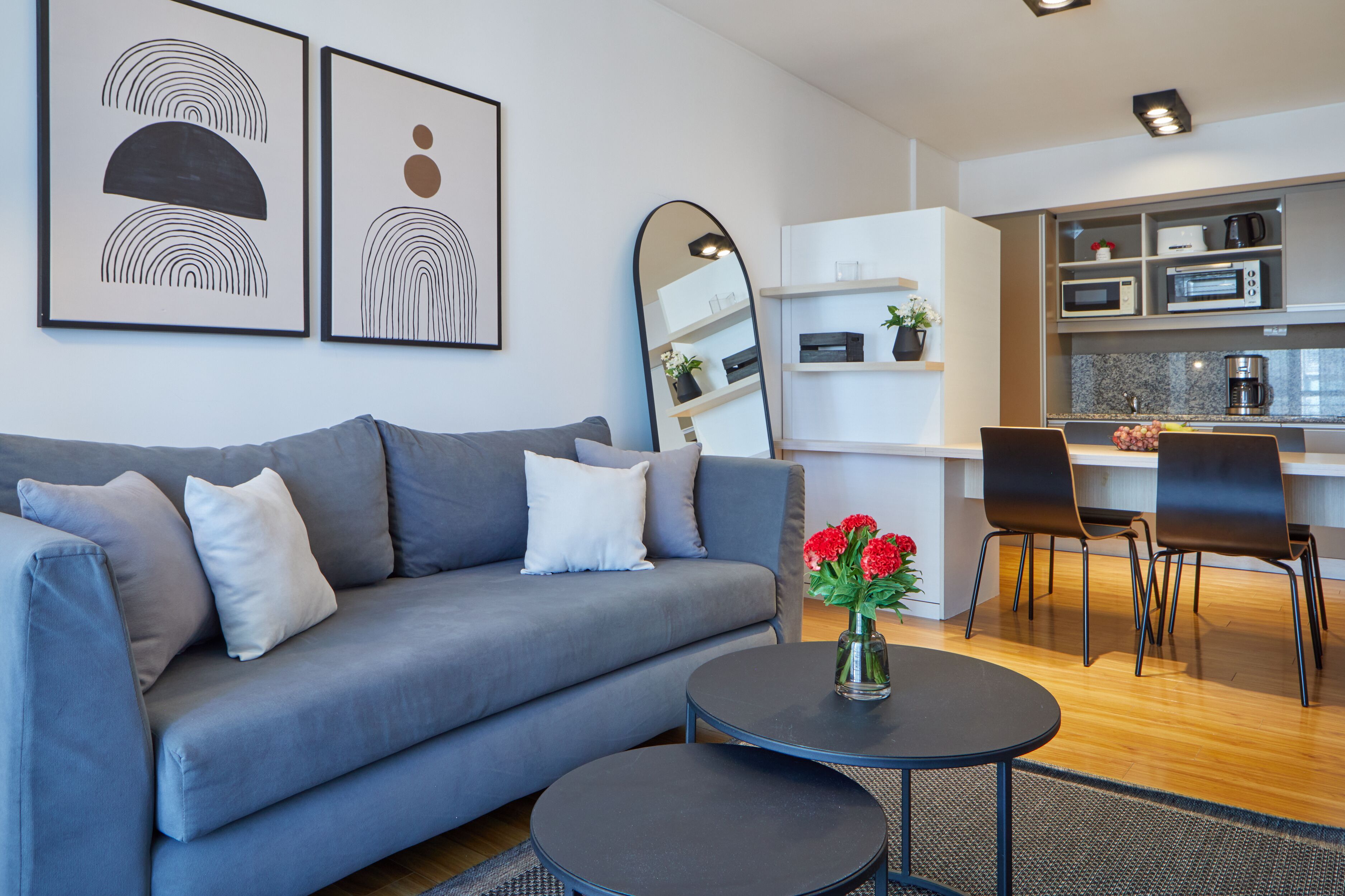 A modern living room with a grey sofa, a coffee table, and a dining area with chairs and a kitchen in the background.