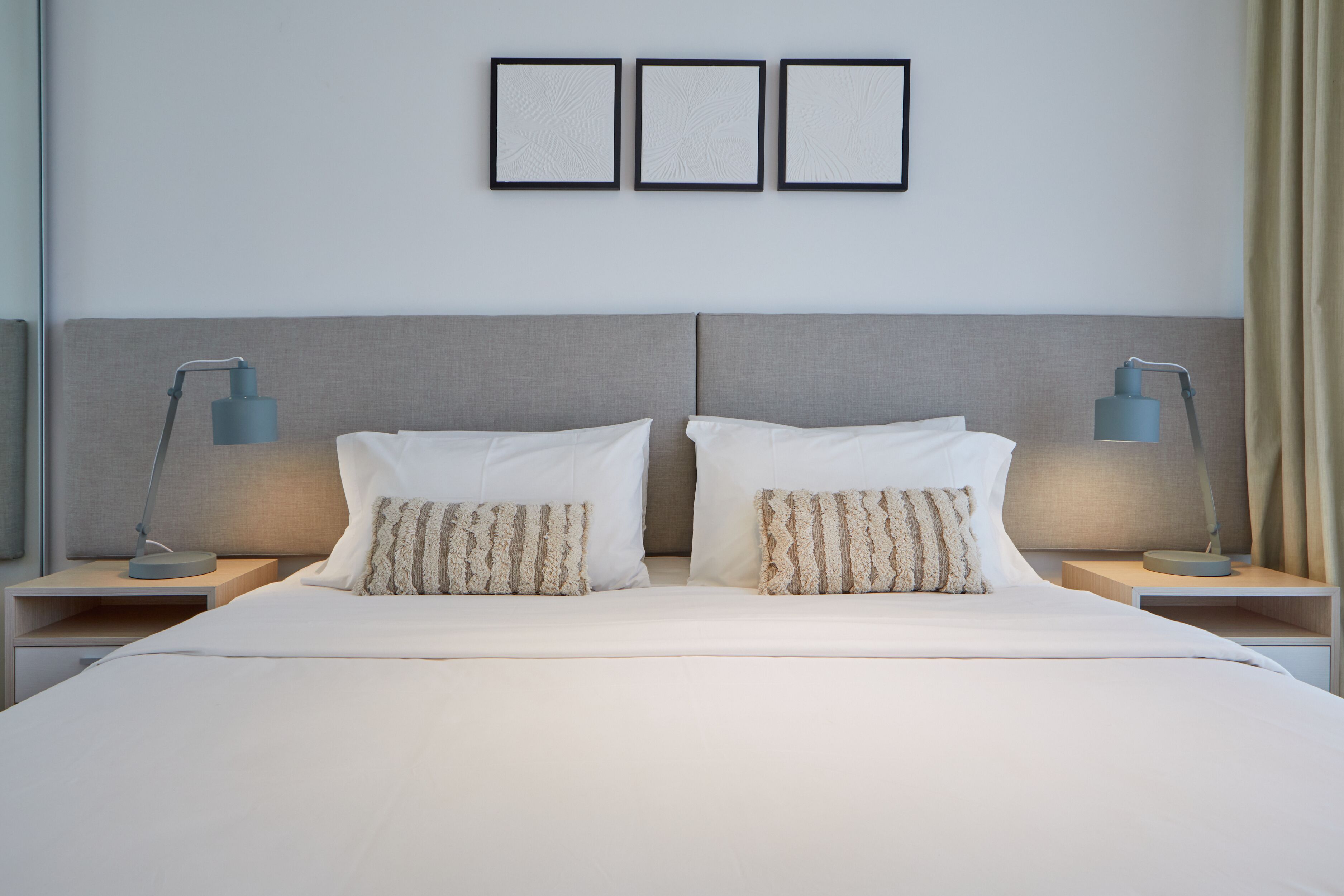 Un lit bien fait, avec du linge de lit blanc et deux coussins décoratifs, flanqué de deux tables de chevet surmontées de lampes, dans une chambre d’hôtel moderne.