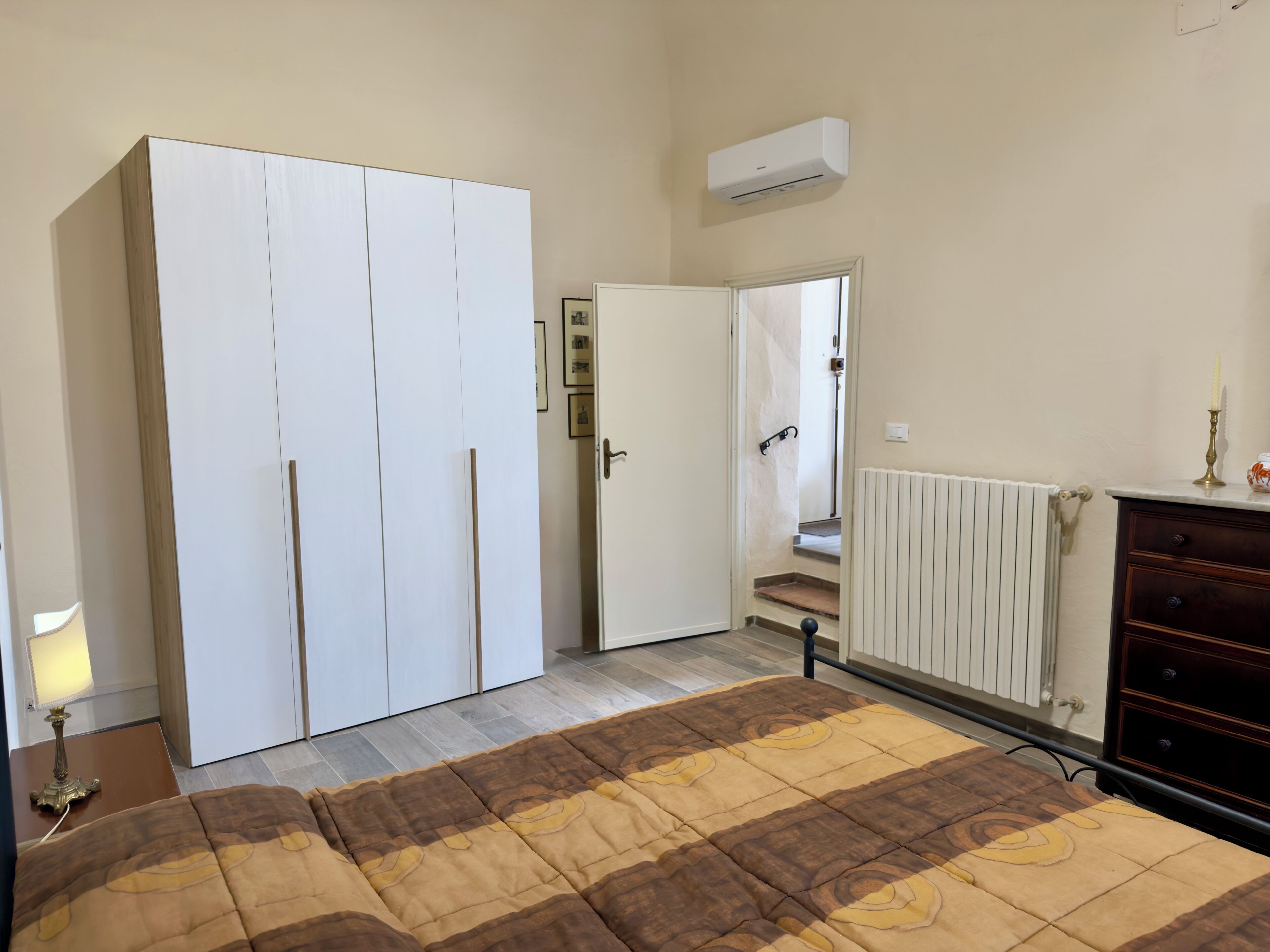 A bedroom with a wardrobe, a radiator, a bedside table with a lamp, and a bed with a patterned bedspread.