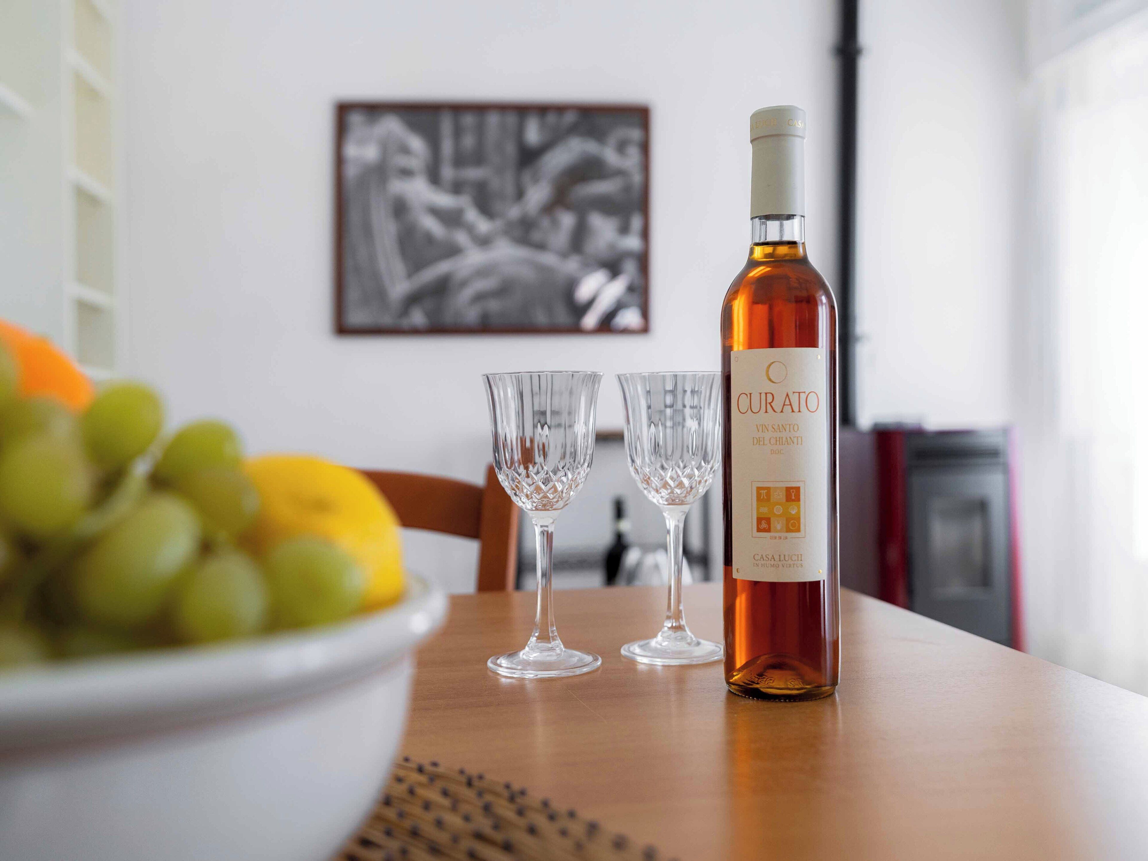Una botella de vino Curato, dos copas de vino vacías y un cuenco con uvas sobre una mesa.