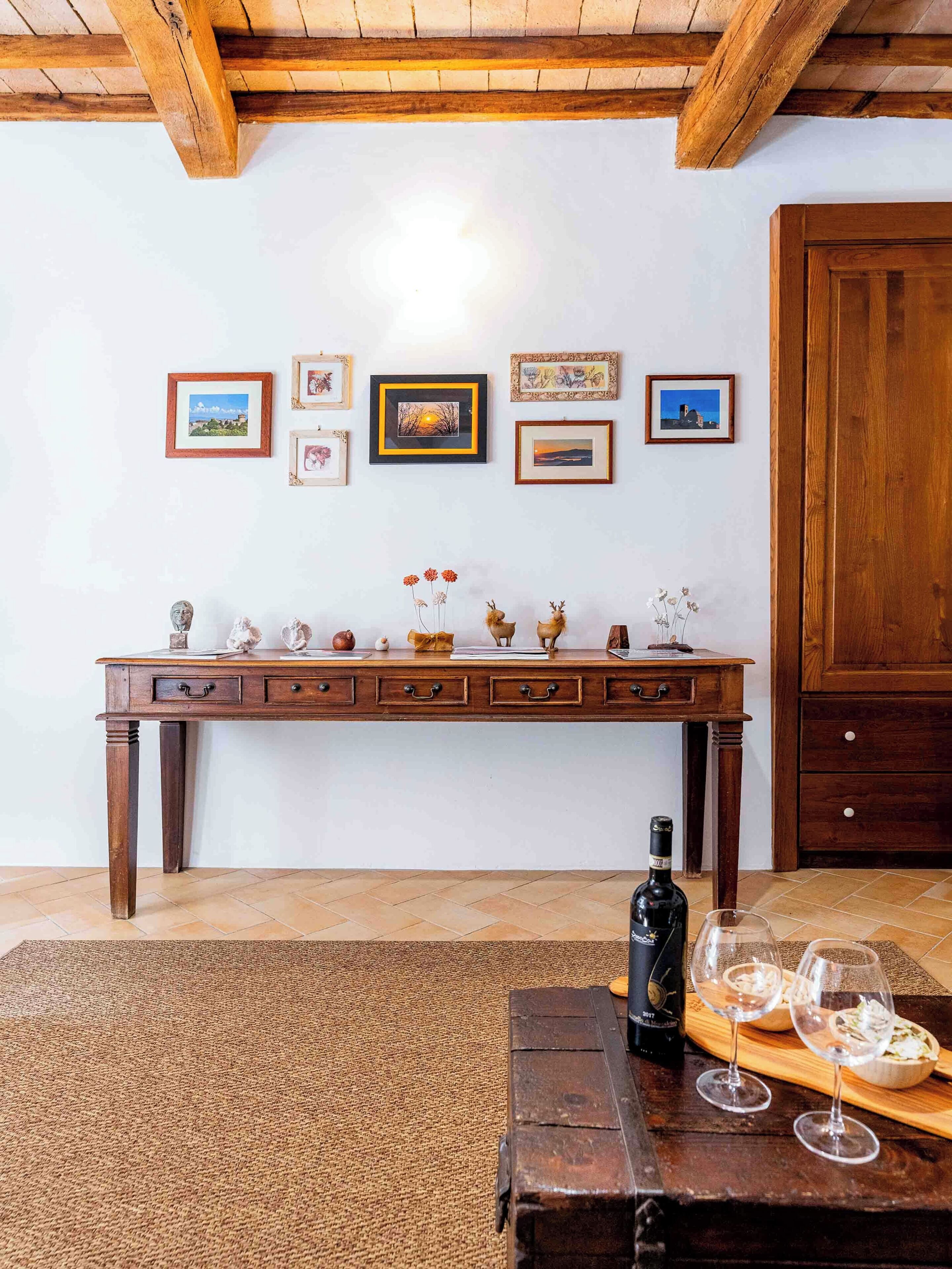 A wooden table with framed pictures, a wooden cabinet, and a bottle of wine on a rug.