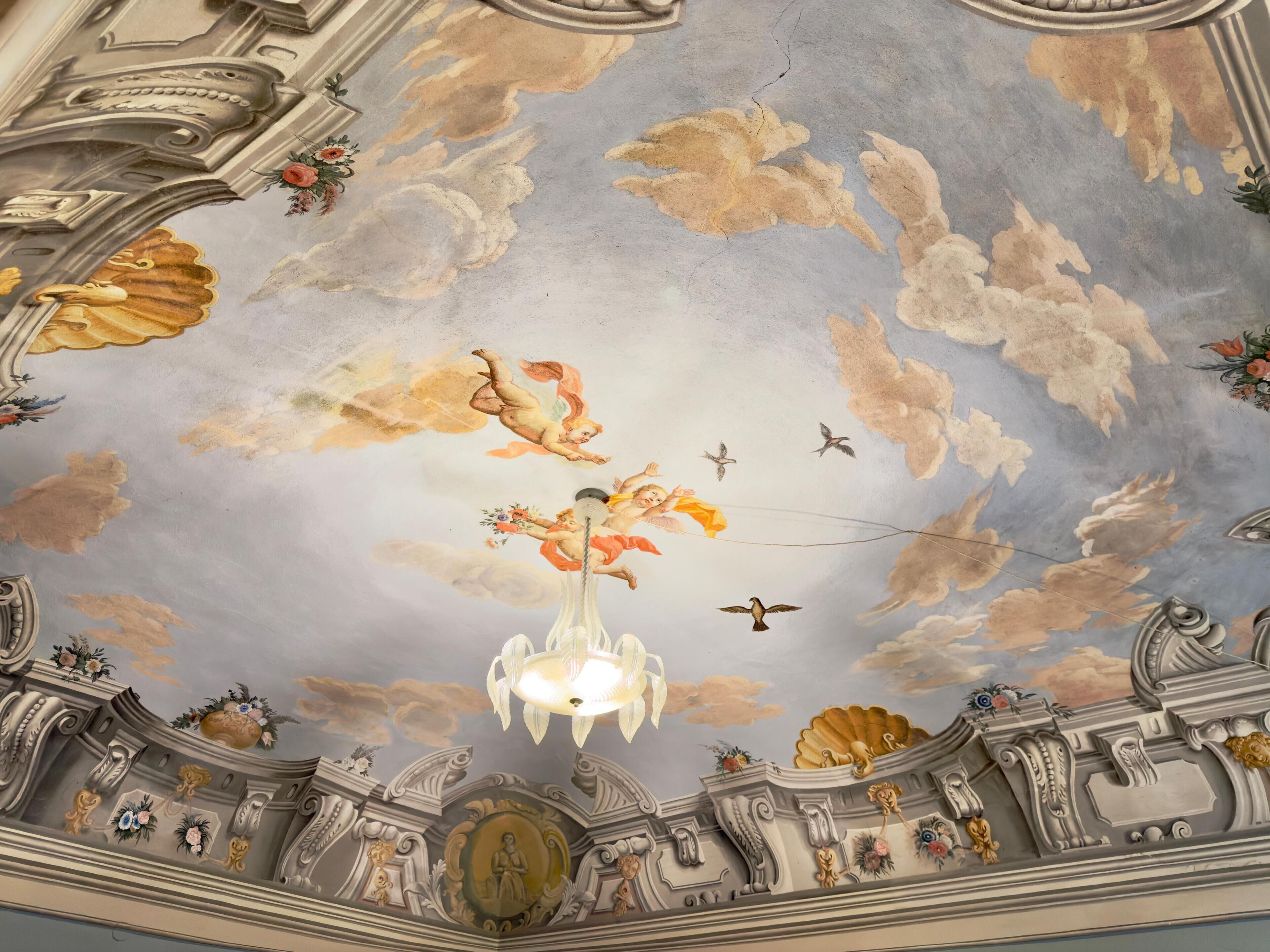 Een plafond met versierde fresco's, een kroonluchter en klassieke architectonische details.