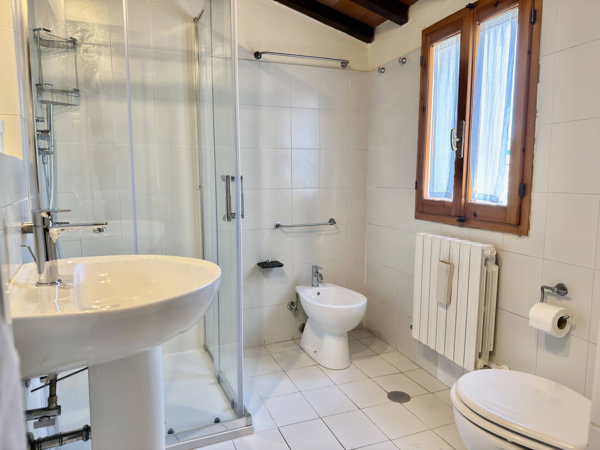 A bathroom with a glass shower enclosure, a white sink, a toilet, and a radiator.