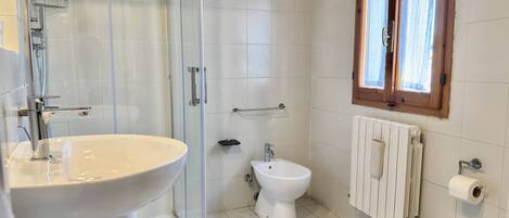 A bathroom with a glass shower enclosure, a white sink, a toilet, and a radiator.