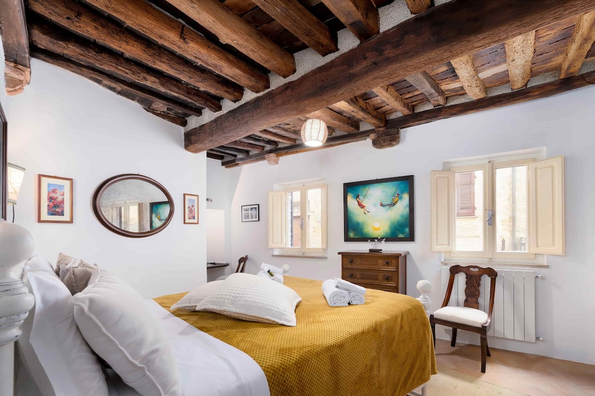 A bedroom with a bed, a dresser, a chair, a mirror, and a painting on the wall.