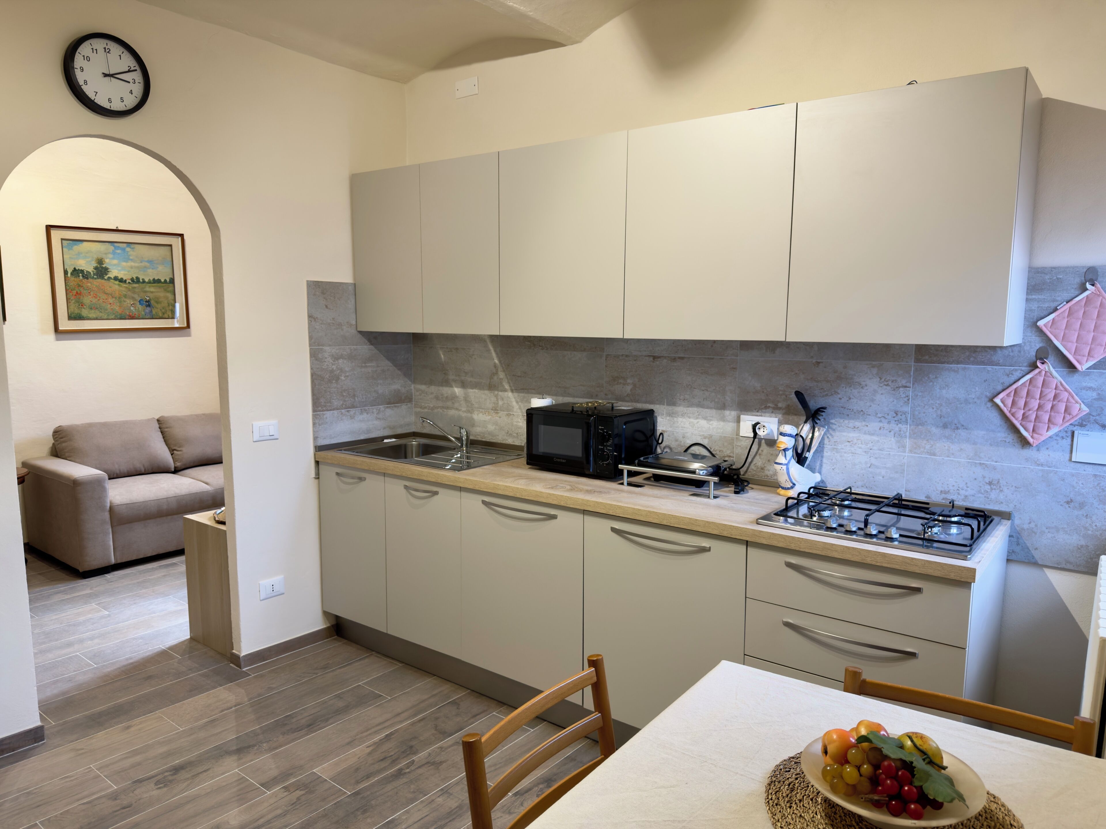 A modern kitchen with a gas stove, microwave, and sink. There is a dining table with a fruit bowl.