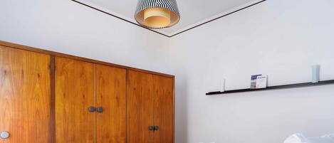 Un dormitorio con un armario de madera, una cama con ropa de cama blanca y un estante pequeño con artículos de aseo.