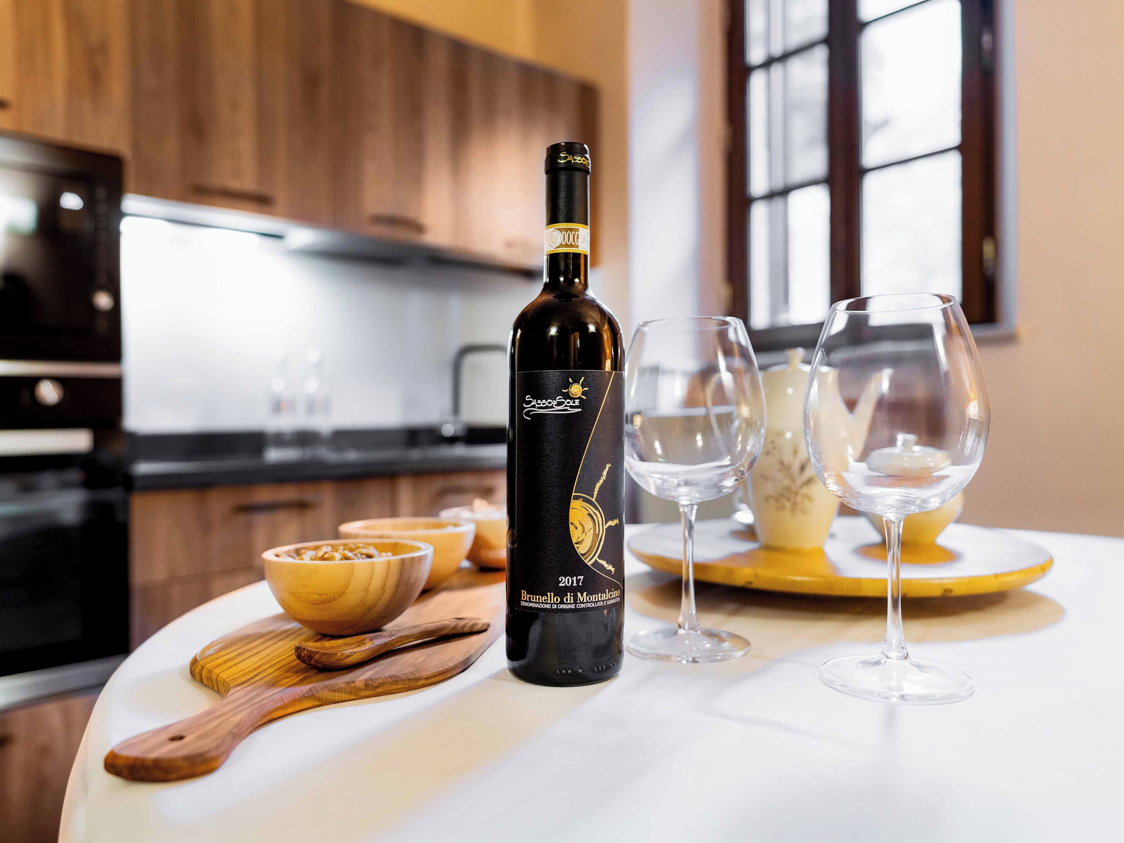 Una bottiglia di vino Brunello di Montalcino su un tavolo con due bicchieri da vino e un tagliere di legno.