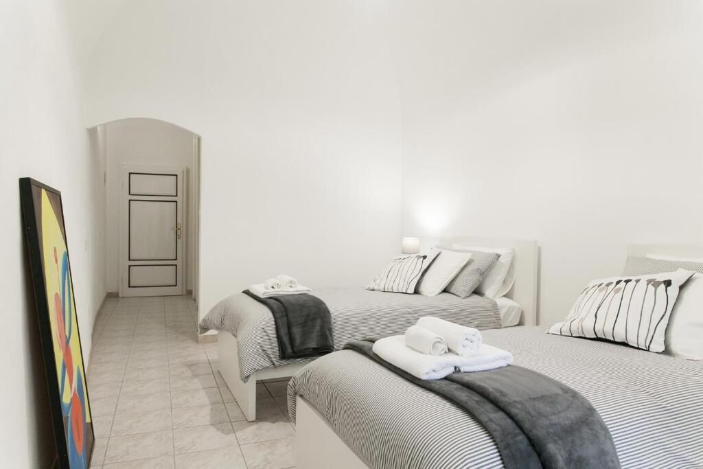 A hotel room with two beds, a painting on the wall, and a door leading to another room.