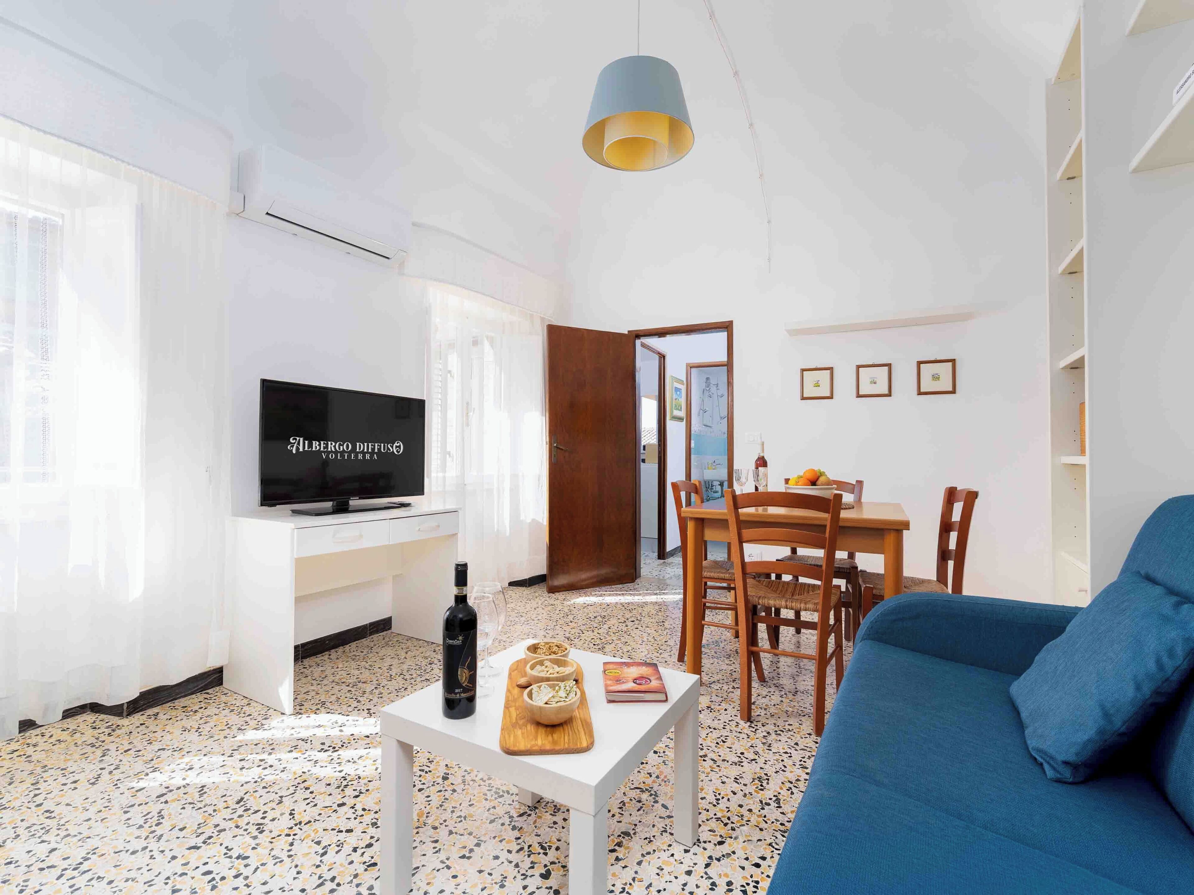 Una sala de estar con televisor, mesa de comedor, sillas, sofá y una pequeña mesa con una botella y vasos.