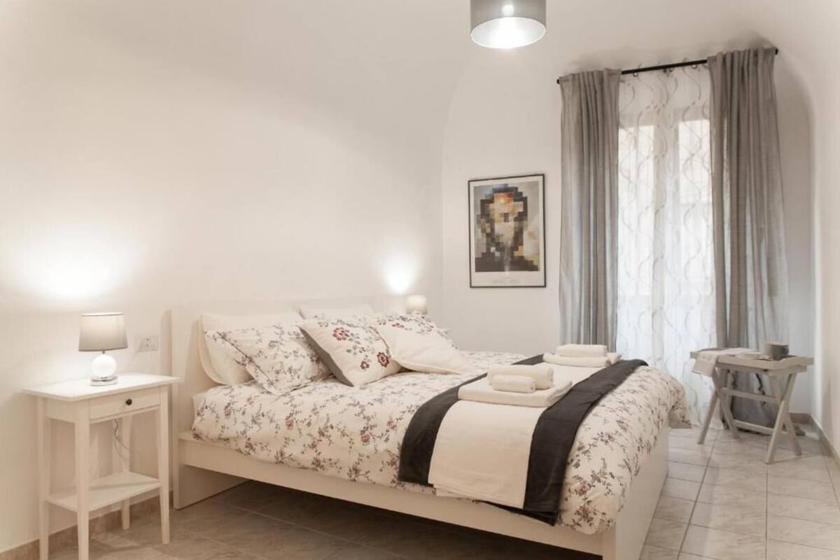 A bedroom with a bed, bedside table, lamp, and a small table with a chair.