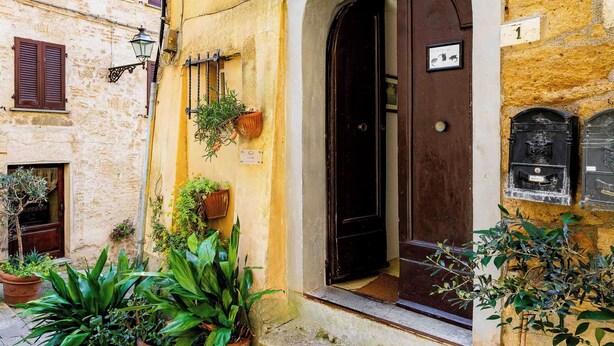 A yellow building with a dark door, potted plants, and a stone staircase leading to the entrance. - AlbergoDiffusoVolterra (Volterra)